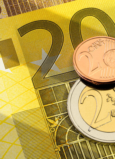 Várias moedas de euro, uma de um euro e outra de um cêntimo, na parte superior de uma nota de 200 euros amarela.
